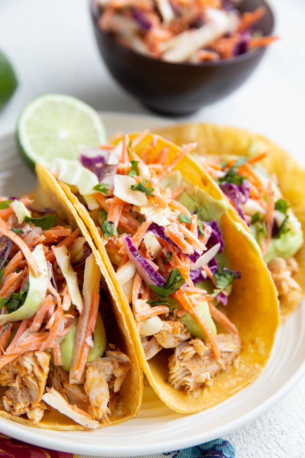 Three fish tacos on a plate with slaw and avocado sauce.