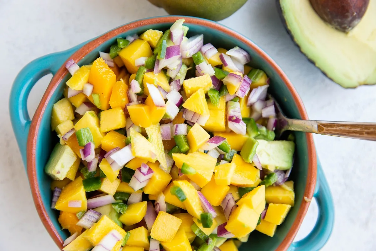 Fresh mango salsa in a blue serving dish with a wooden spoon, ready to serve.