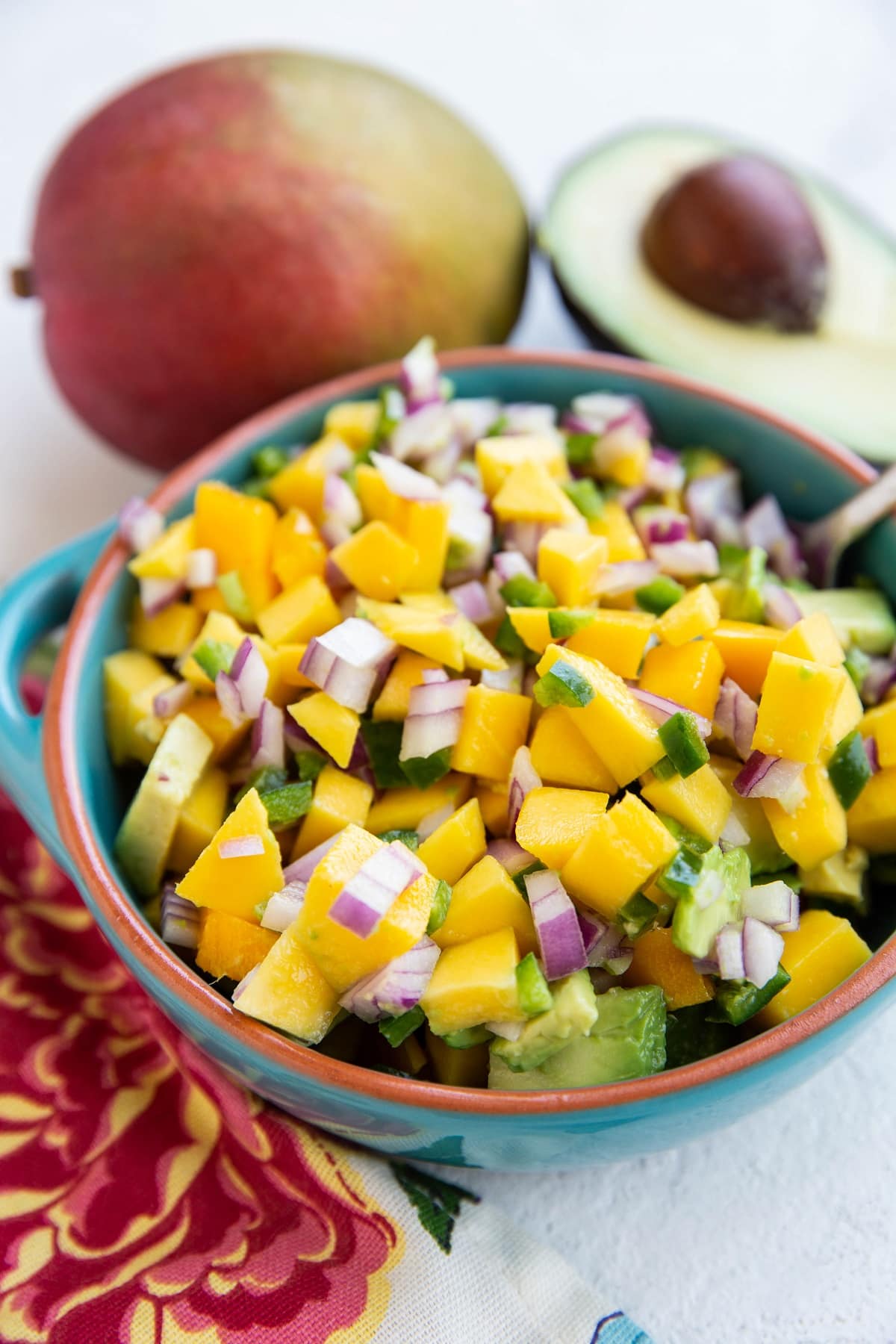 Bowl of mango avocado salsa with fresh ripe mangoes and ripe avocados in the background.