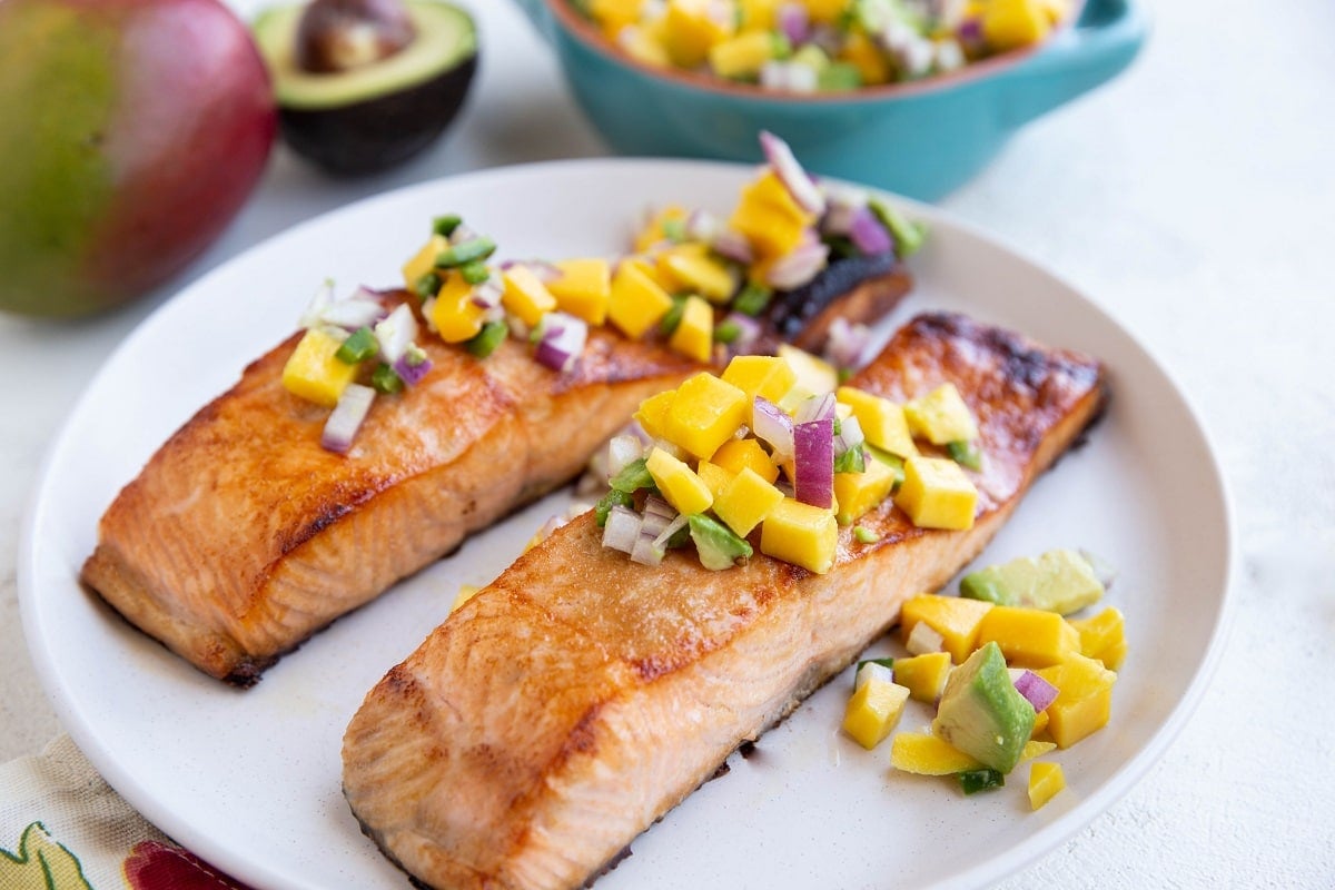 Two seared salmon filets on a plate with mango salsa on top.