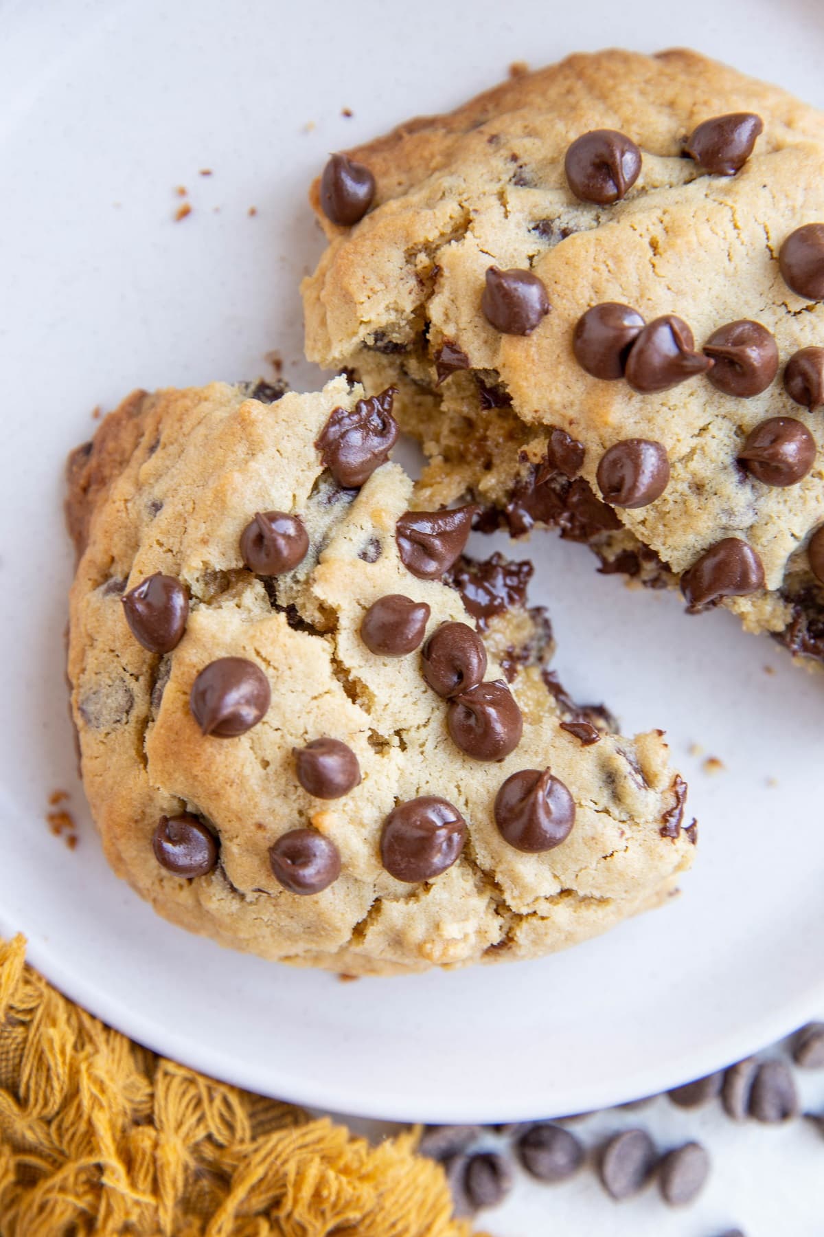 One big chocolate chip cookie broken in half on a white plate.