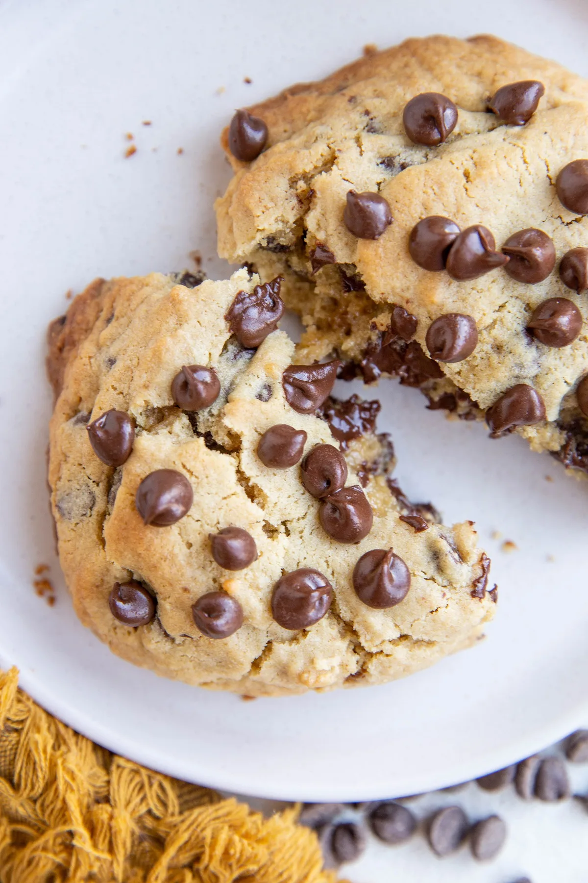 One big chocolate chip cookie broken in half on a white plate.