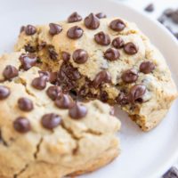 One giant chocolate chip cookie on a white plate, broken in half to expose the gooey center.