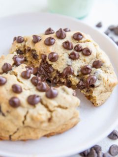 One giant chocolate chip cookie on a white plate, broken in half to expose the gooey center.