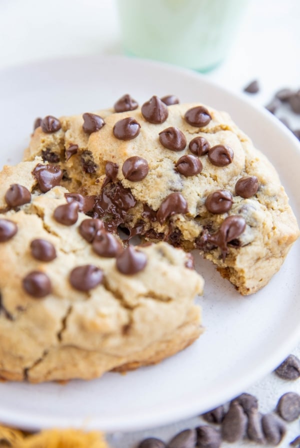 One giant chocolate chip cookie on a white plate, broken in half to expose the gooey center.