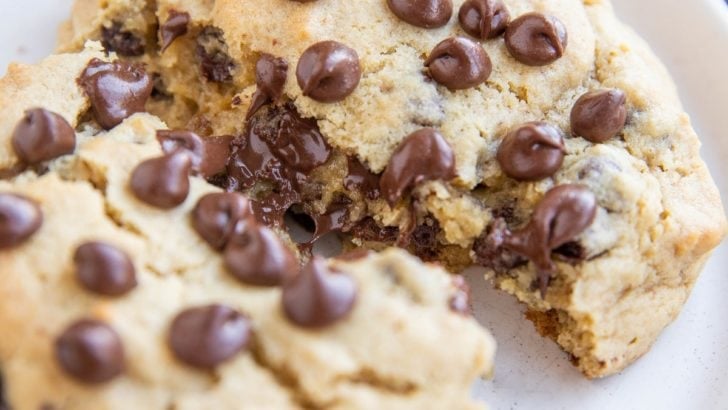 One giant chocolate chip cookie on a white plate, broken in half to expose the gooey center.