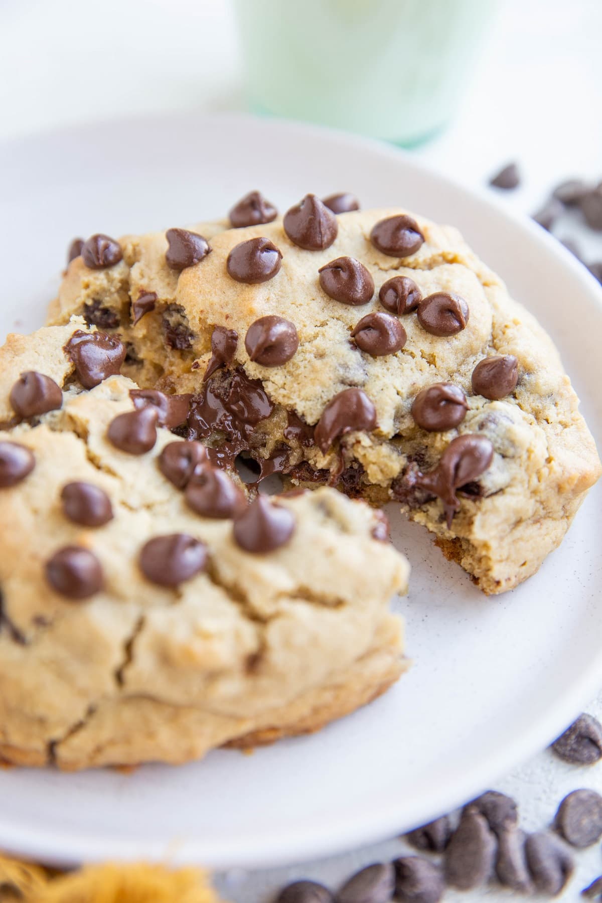 One giant chocolate chip cookie on a white plate, broken in half to expose the gooey center.