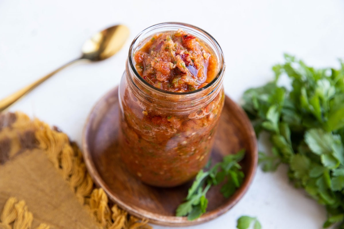 Mason jar of homemade salsa on a wooden plate with fresh cilantro to the side.