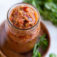 Red salsa in a jar with fresh cilantro in the background.