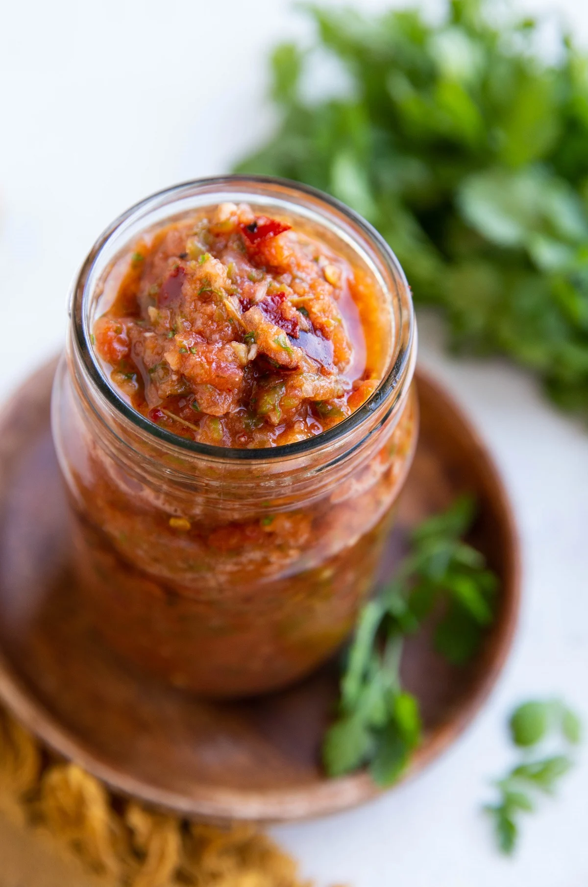 Red salsa in a jar with fresh cilantro in the background.