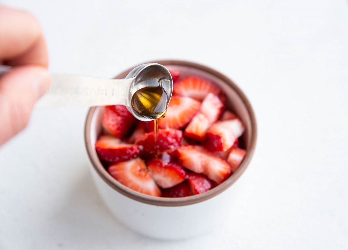 Pouring pure maple syrup into the ramekin with the strawberries.