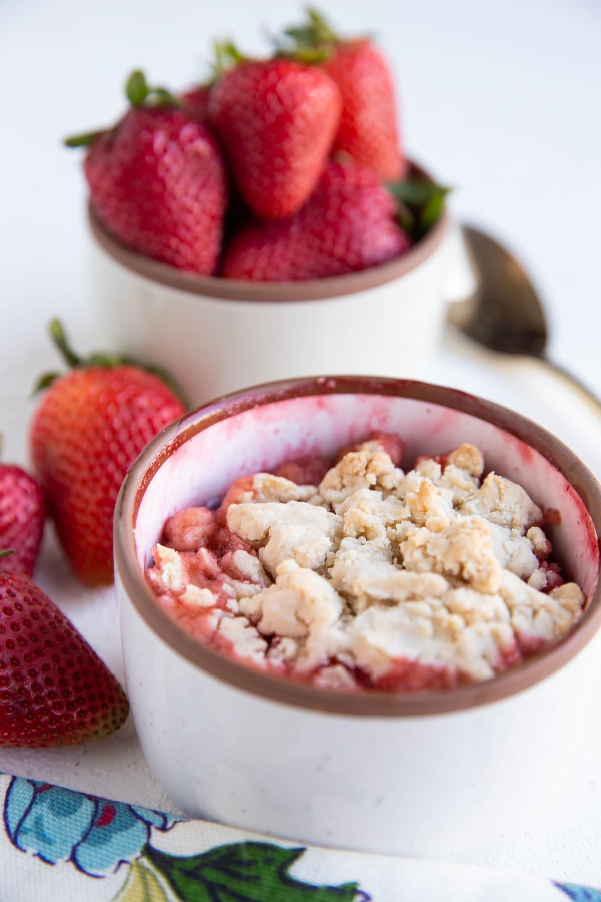 Single Serve Strawberry Cobbler in a white ramekin with fresh strawberries in the background.