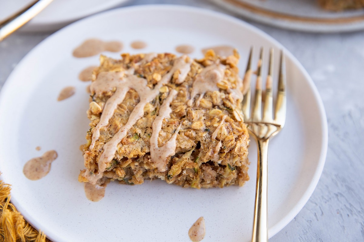 Slice of baked oatmeal on a plate, drizzled with a glaze with a golden fork to the side.