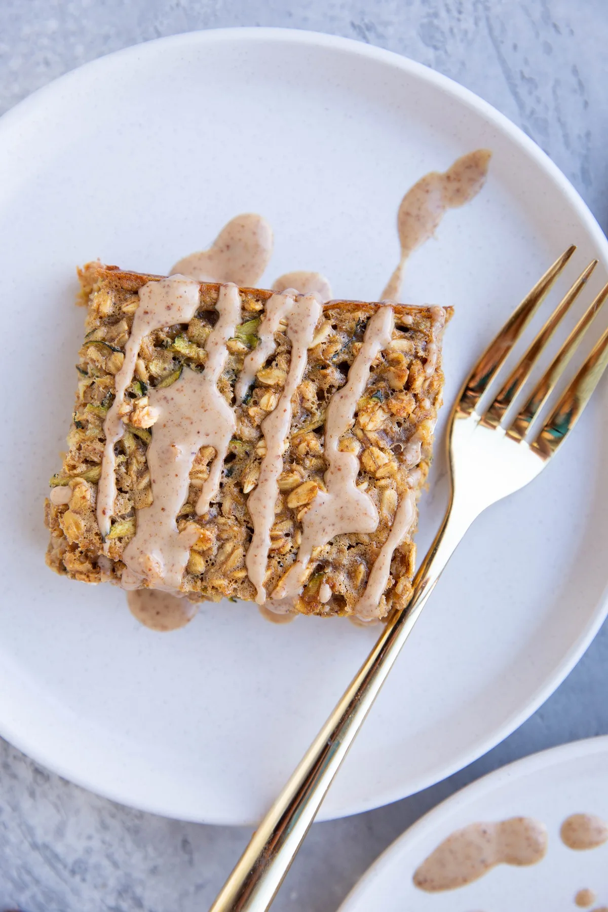 Slice of baked oatmeal on a white plate, drizzled with an almond butter glaze.