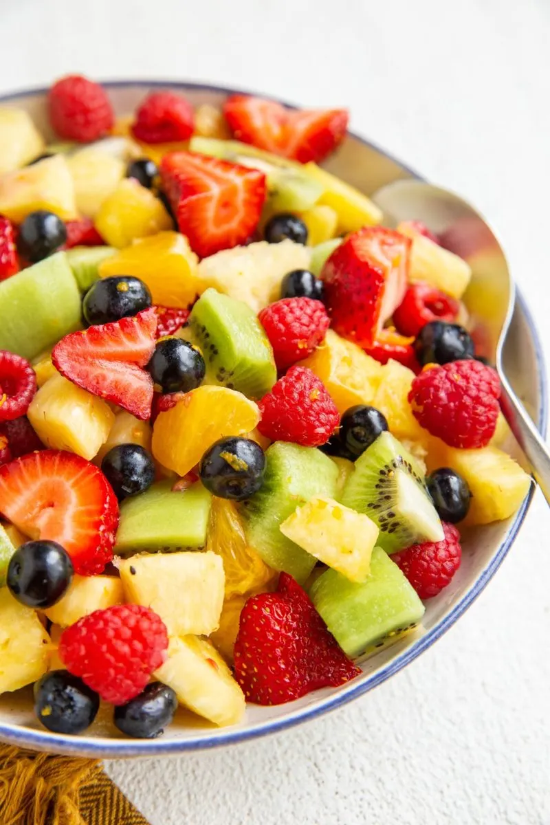 Blue rimmed bowl of fruit salad with a serving spoon.