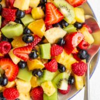 Blue rimmed white bowl full of the best fruit salad with a silver serving spoon.