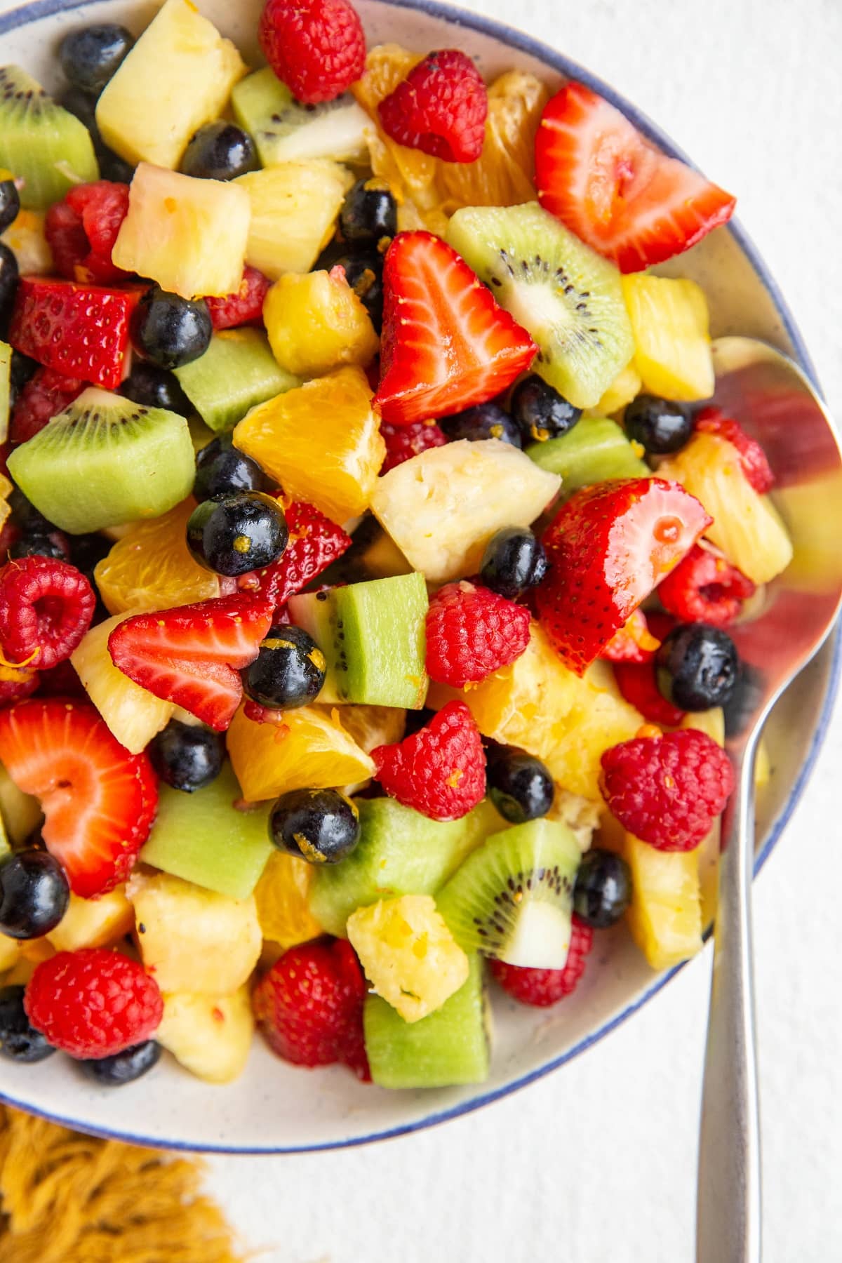 Blue rimmed white bowl full of the best fruit salad with a silver serving spoon.