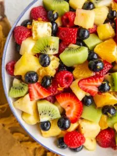 Big bowl of fruit salad with a citrus dressing in a blue rimmed white serving bowl.