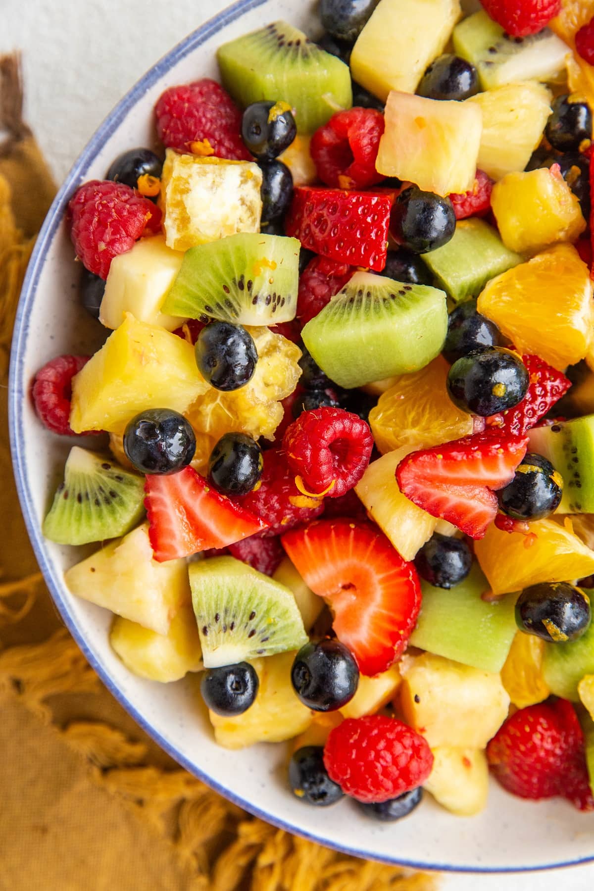 Big bowl of fruit salad with a citrus dressing in a blue rimmed white serving bowl.