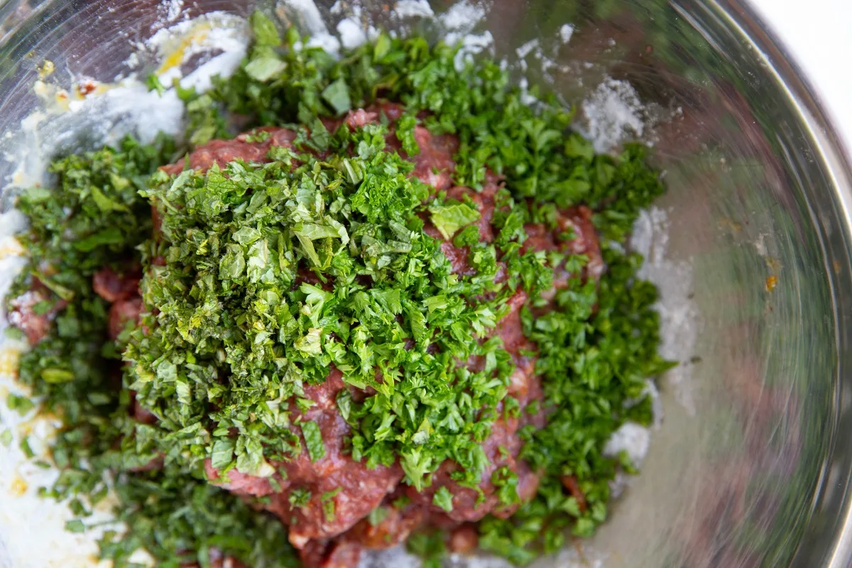 Fresh herbs on top of meatball mixture, to be mixed in.