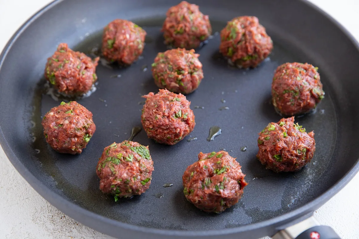 Meatballs searing on a skillet to be browned.