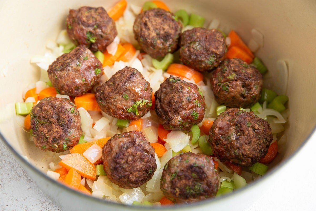 Meatballs on top of veggies in a soup pot.