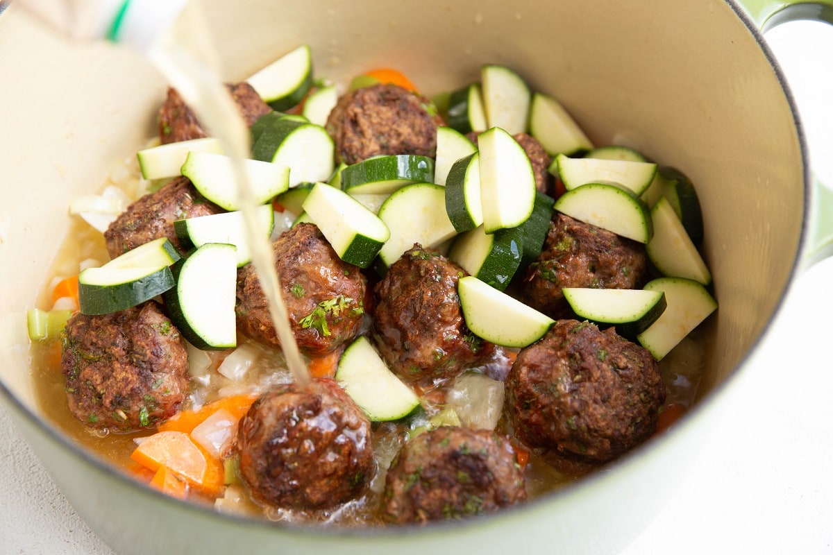 Pouring broth into the soup pot with the other ingredients.