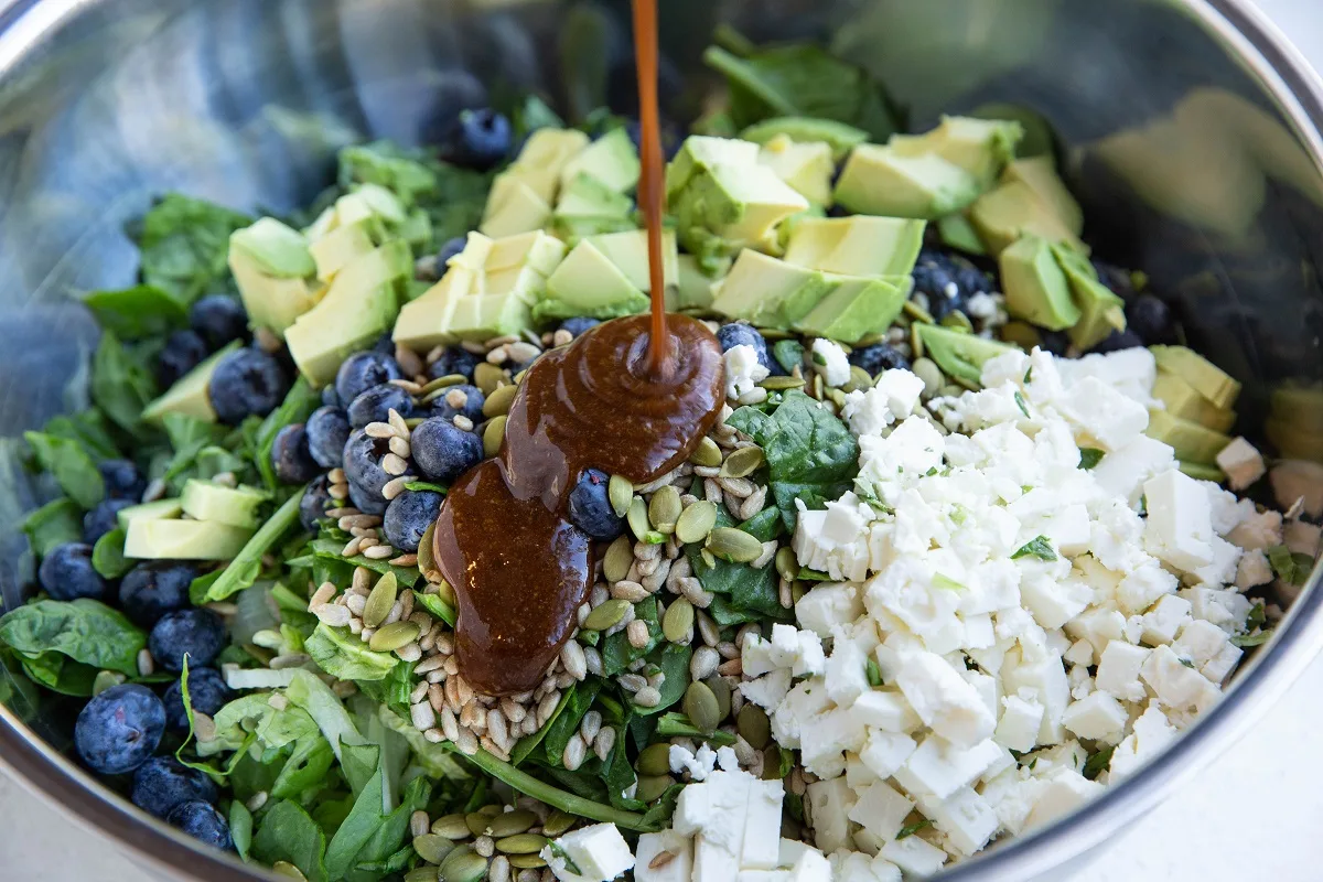 Drizzling balsamic vinaigrette into the bowl with the salad ingredients.