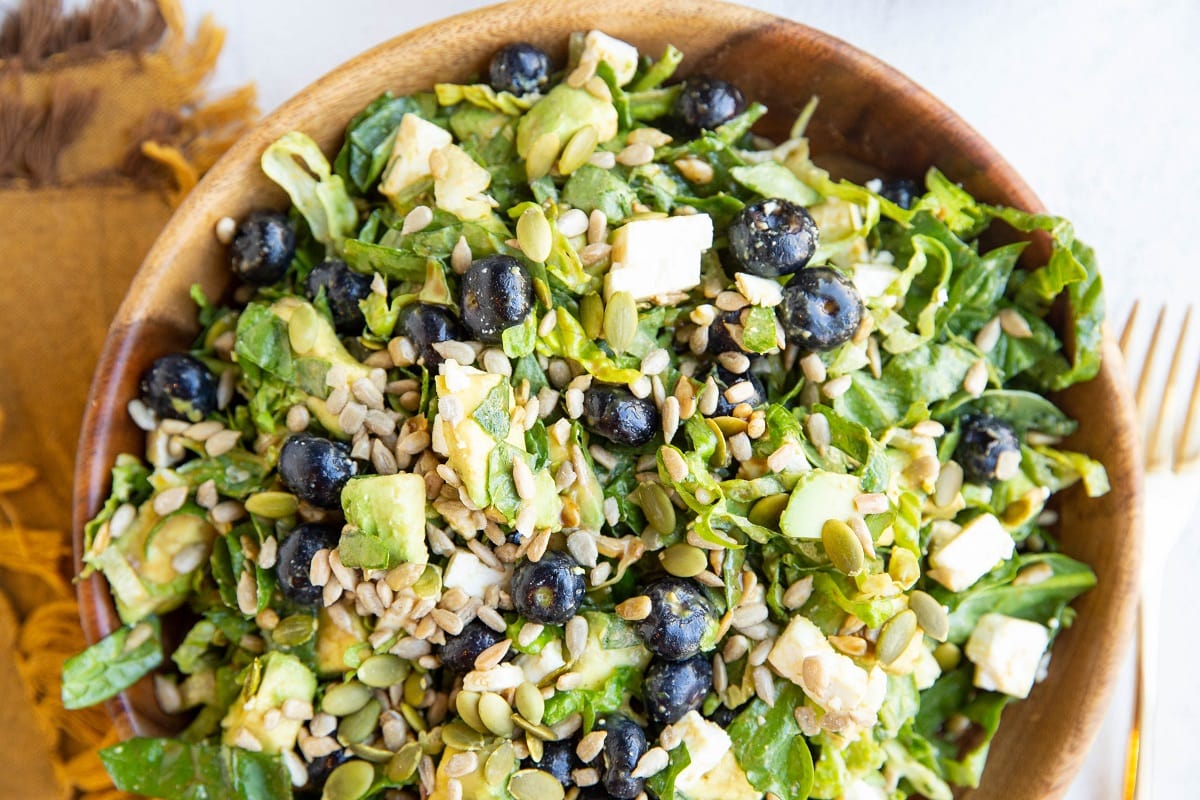 Big wooden bowl of chopped salad with a gold fork and napkin to the side.