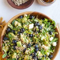 Bowl of green salad with blueberries, avocado, sunflower seeds, feta cheese, pumpkin seeds and balsamic vinaigrette mixed in.