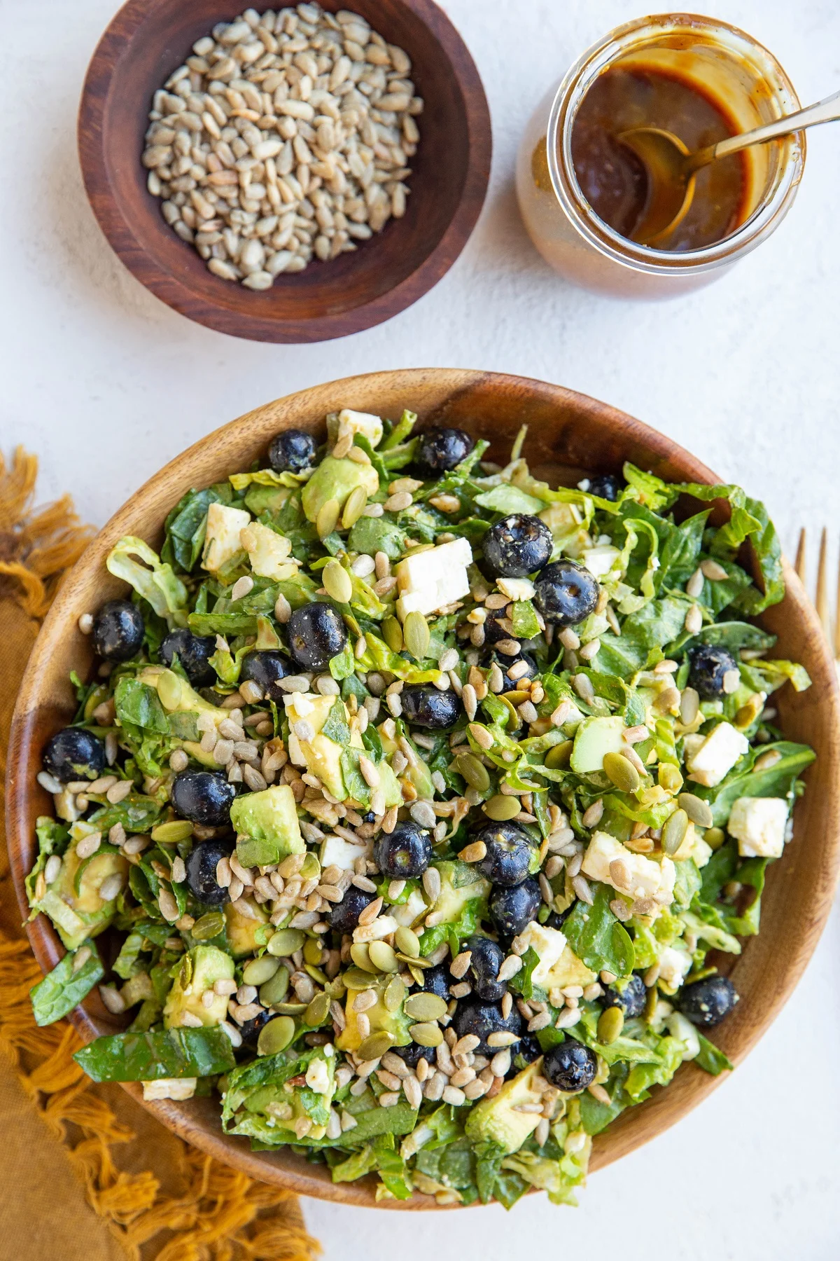 Bowl of green salad with blueberries, avocado, sunflower seeds, feta cheese, pumpkin seeds and balsamic vinaigrette mixed in.
