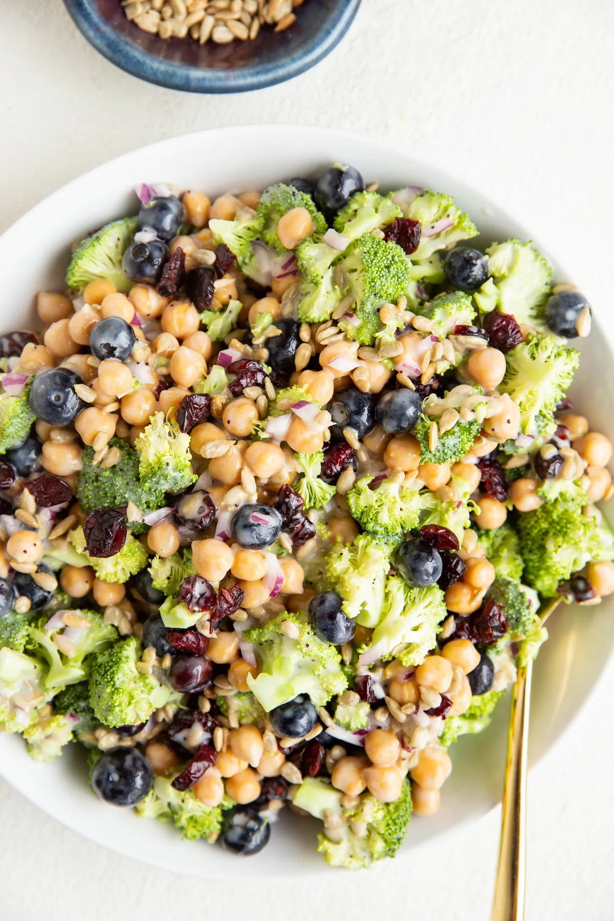 White serving bowl of broccoli salad with garbanzo beans and more.