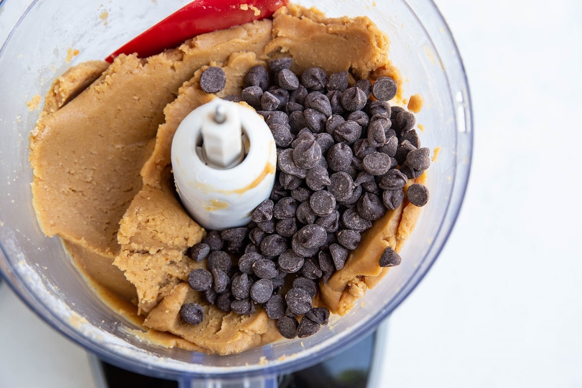 Chickpea peanut butter cookie dough in a food processor with chocolate chips on top, ready to be mixed in.