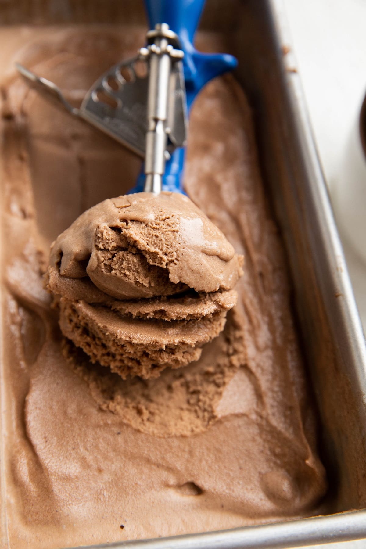 Container of dairy-free chocolate ice cream with an ice cream scoop scooping one scoop of ice cream.
