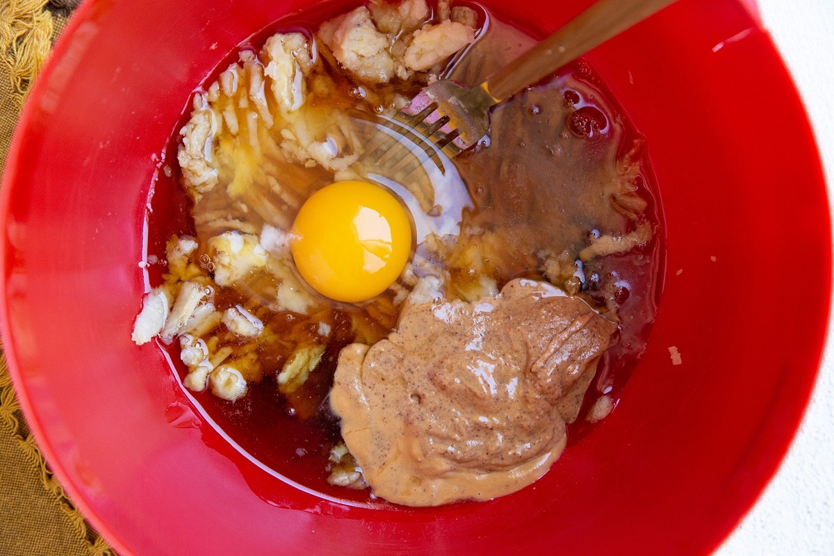 Red mixing bowl with mashed sweet potato, almond butter, pure maple syrup and egg inside.