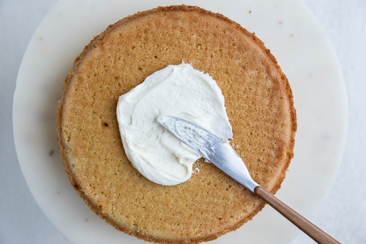 Vanilla cake with vanilla buttercream being spread on top.