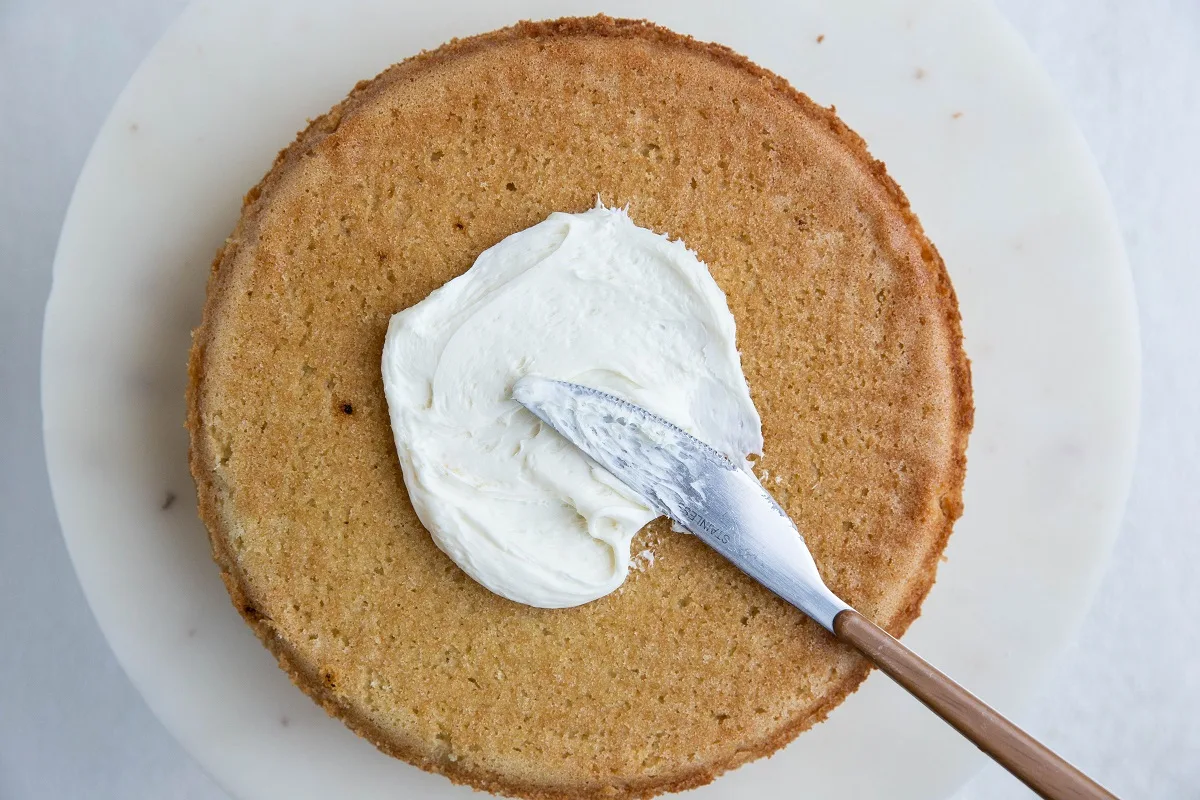 Vanilla cake with vanilla buttercream being spread on top.