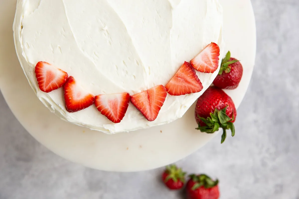 Frosted vanilla cake on a cake stand with sliced strawberries on top