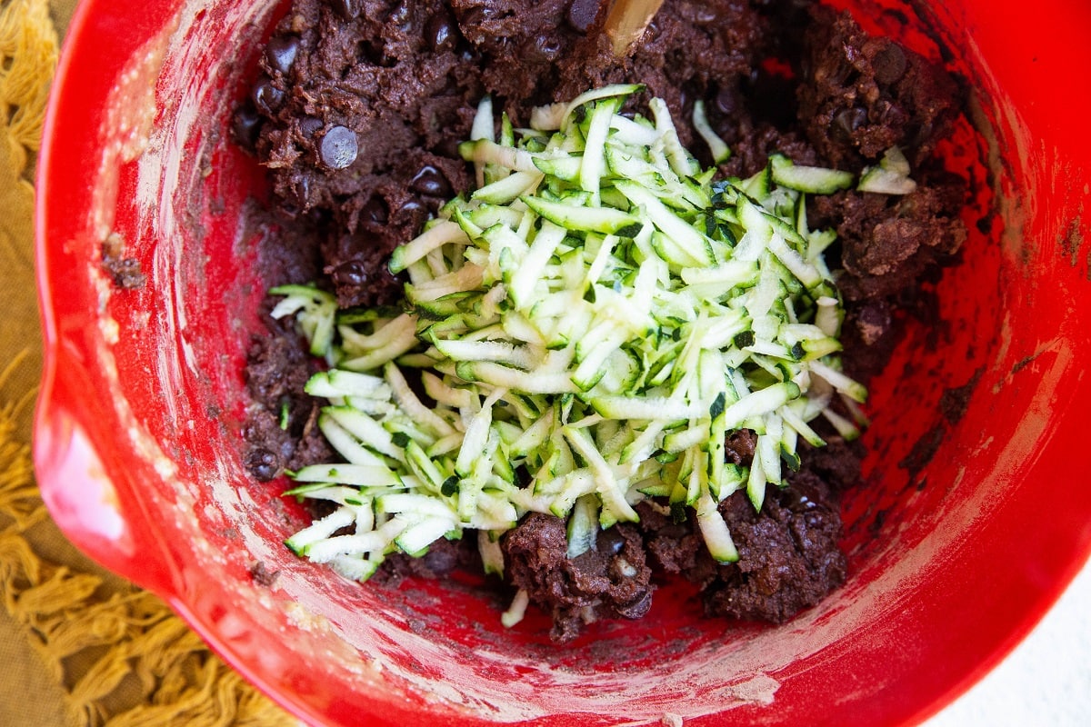 Brownie batter in a mixing bowl with grated zucchini on top ready to be mixed in.