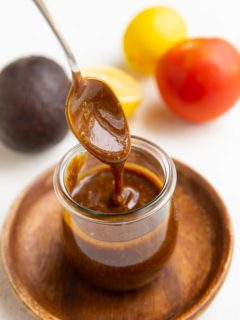 Spoon drizzling balsamic vinaigrette in a jar with fresh produce in the background.