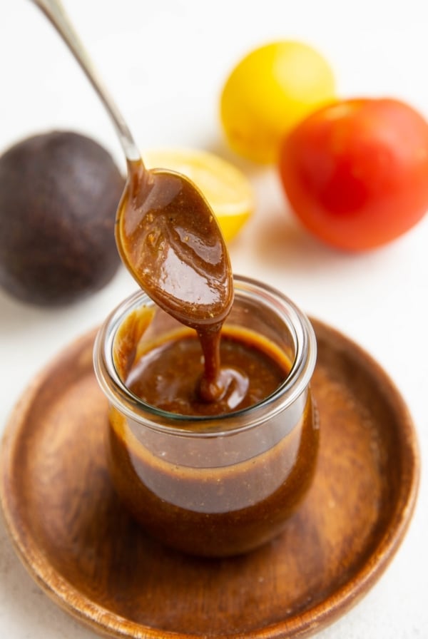 Spoon drizzling balsamic vinaigrette in a jar with fresh produce in the background.