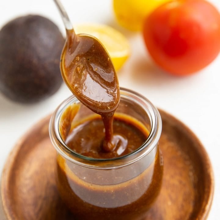 Spoon drizzling balsamic vinaigrette in a jar with fresh produce in the background.