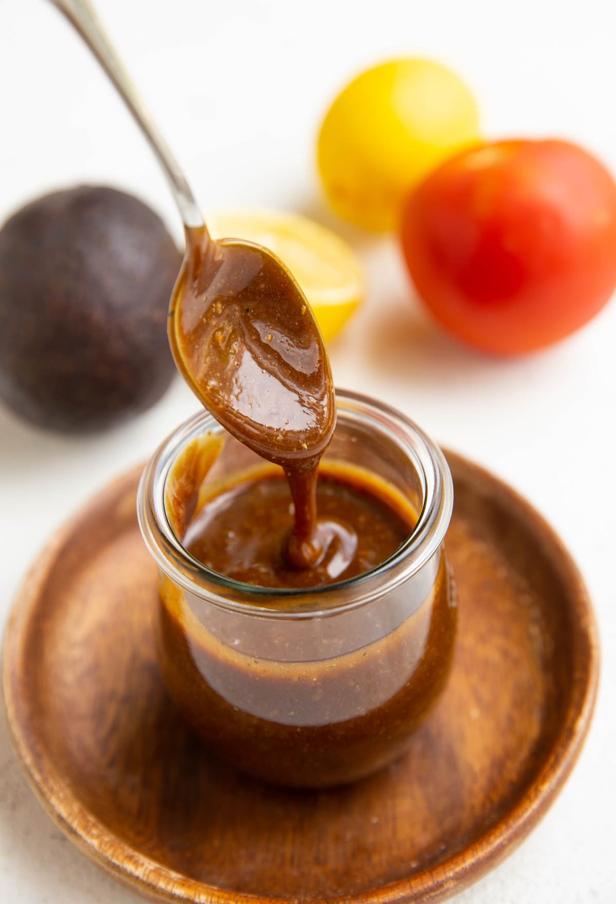 Spoon drizzling balsamic vinaigrette in a jar with fresh produce in the background.