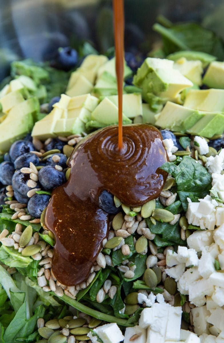 Drizzling balsamic dressing into a mixing bowl with salad ingredients to toss the salad.