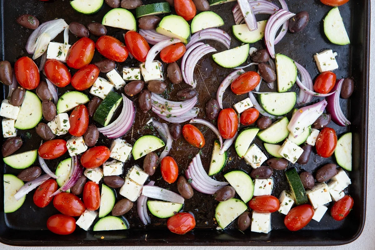 Vegetables tossed in oil and seasonings in a single layer on a sheet pan.