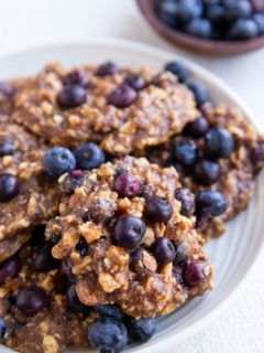 White plate of blueberry banana cookies with fresh blueberries all around.