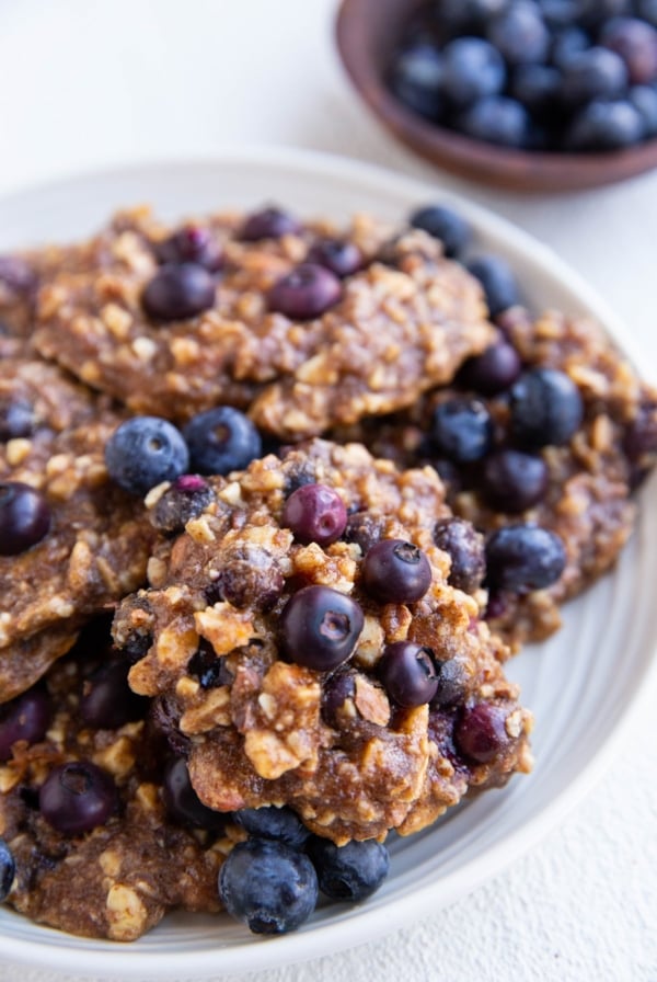 White plate of blueberry banana cookies with fresh blueberries all around.