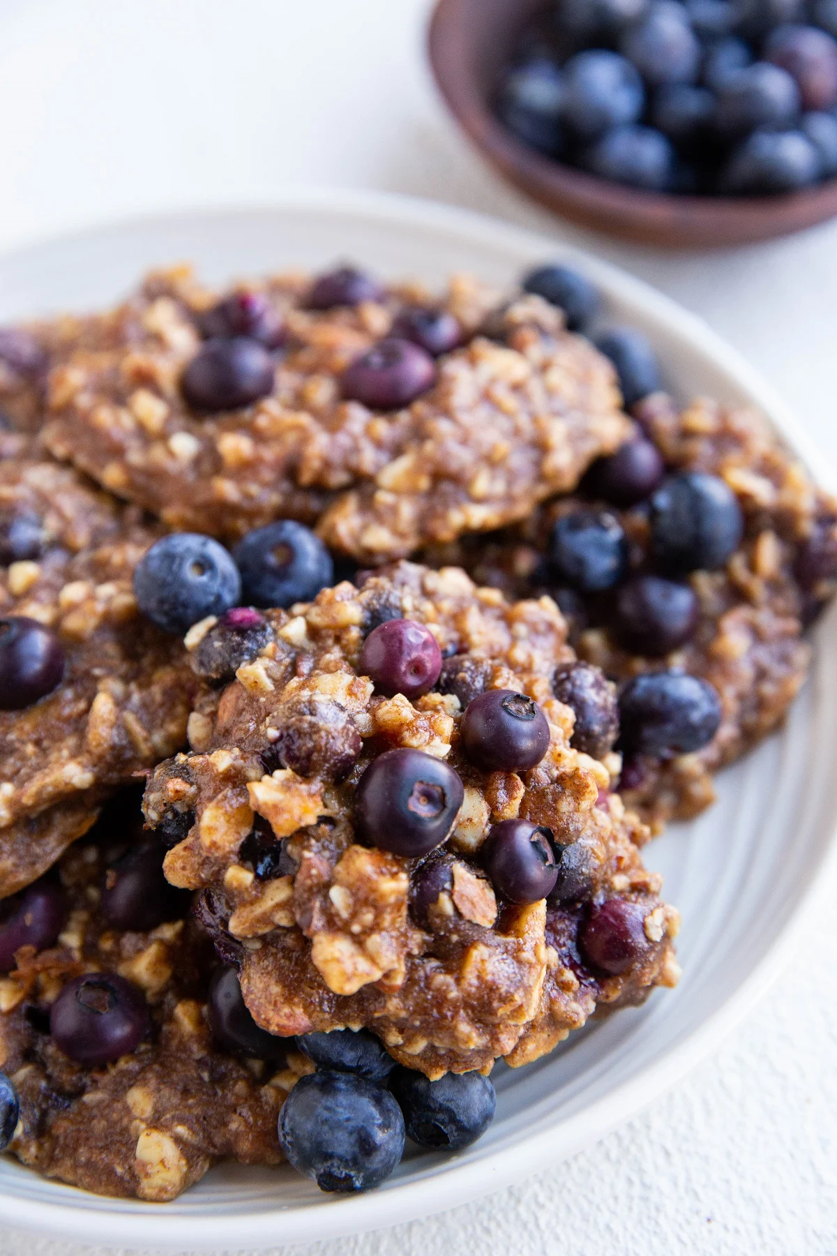 White plate of blueberry banana cookies with fresh blueberries all around.