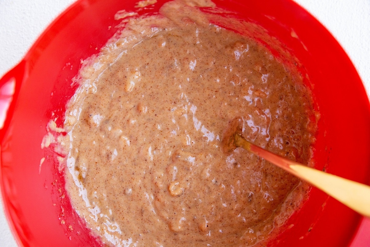 Mashed banana and almond butter in a red mixing bowl.