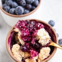 White ramekin with blueberry cobbler and a bowl of fresh blueberries in the background.